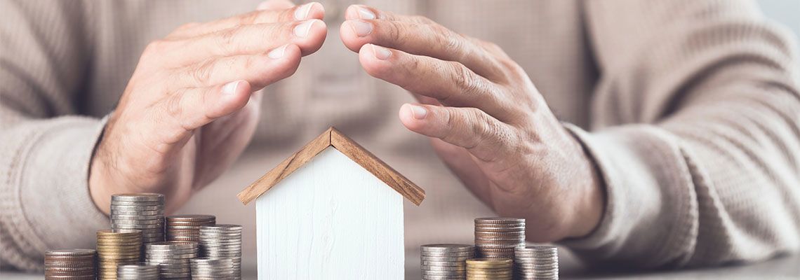 Businessman making a protective hand gesture over house and coin stack