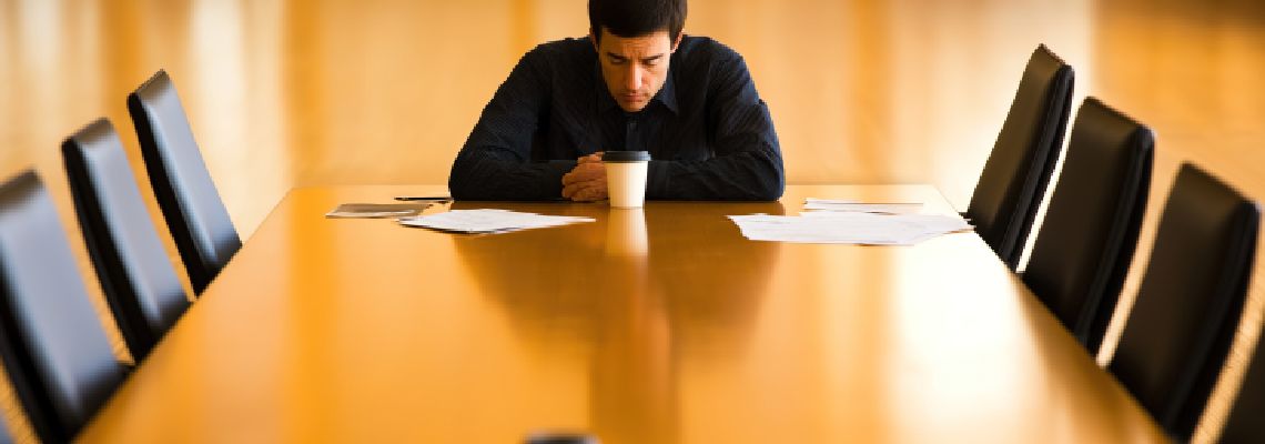 Man sitting alone at large empty conference table with sad expression