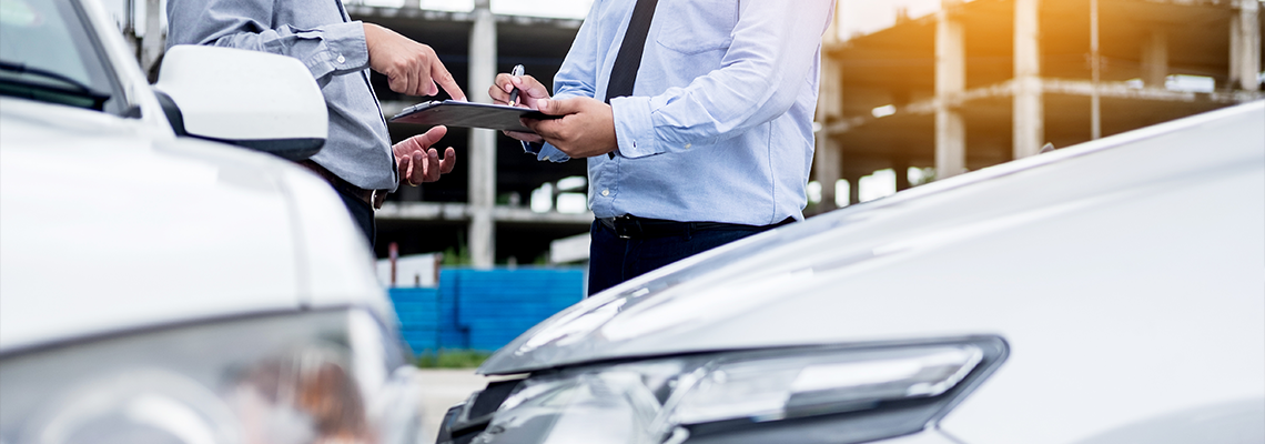 Insurance Agent Writing on Clipboard While Examining Car After Accident