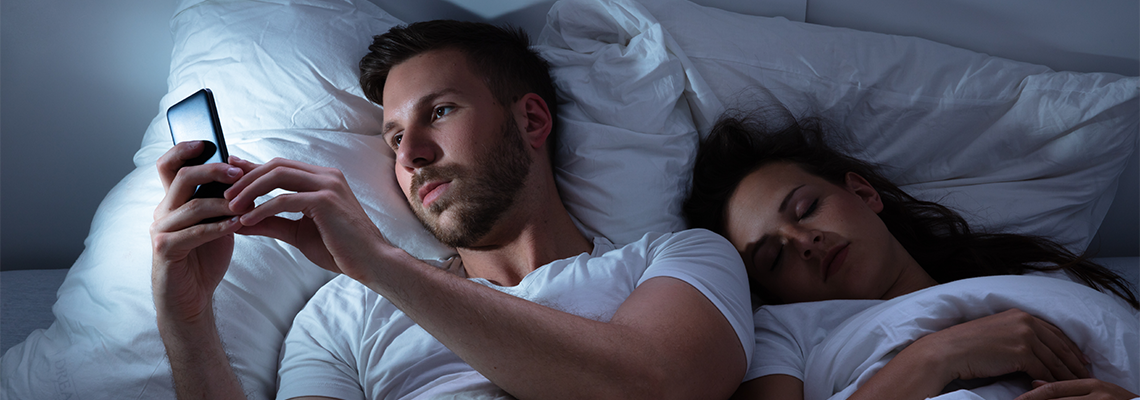 Man Using Cellphone While Her Wife Sleeping On Bed