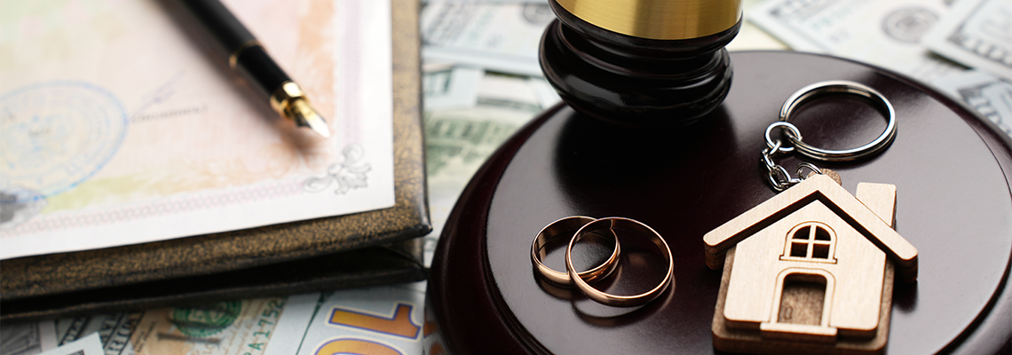 Gold wedding rings, wooden house model, and a judge gavel on legal paperwork