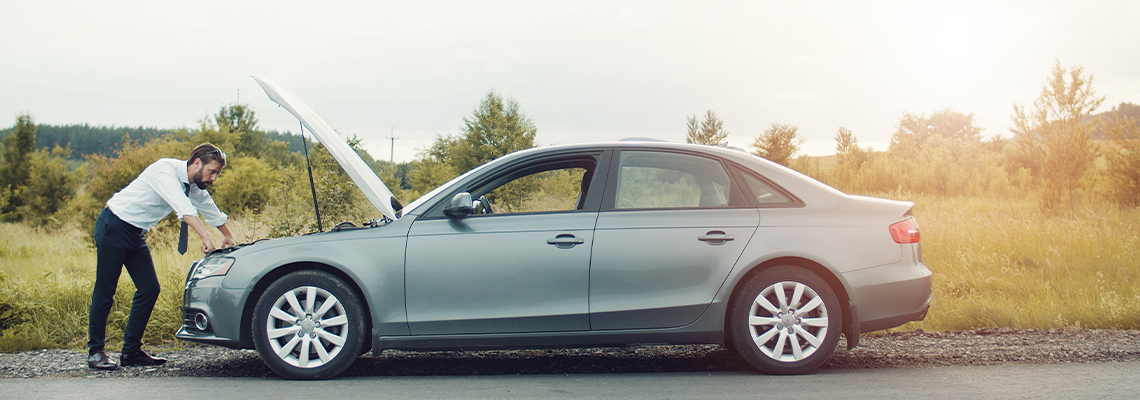 Businessman examining broken down car looking at engine