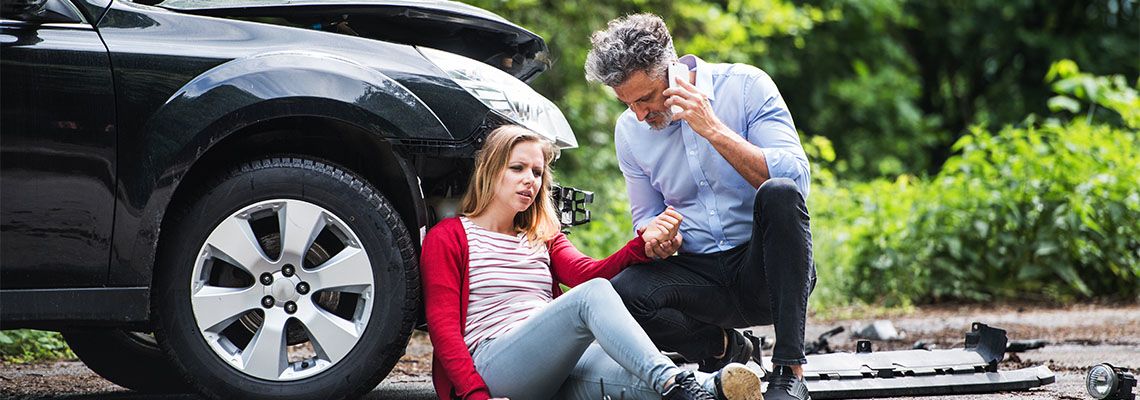 Man on phone besides an Injured woman after car crash