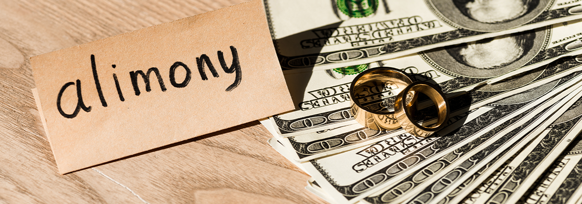 Paper with alimony lettering near dollar banknotes and engagement rings