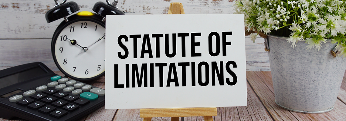 Statute of Limitations text with alarm clock and calculator on wooden background