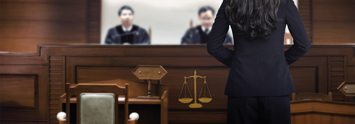 Person standing in courtroom alone across from judges
