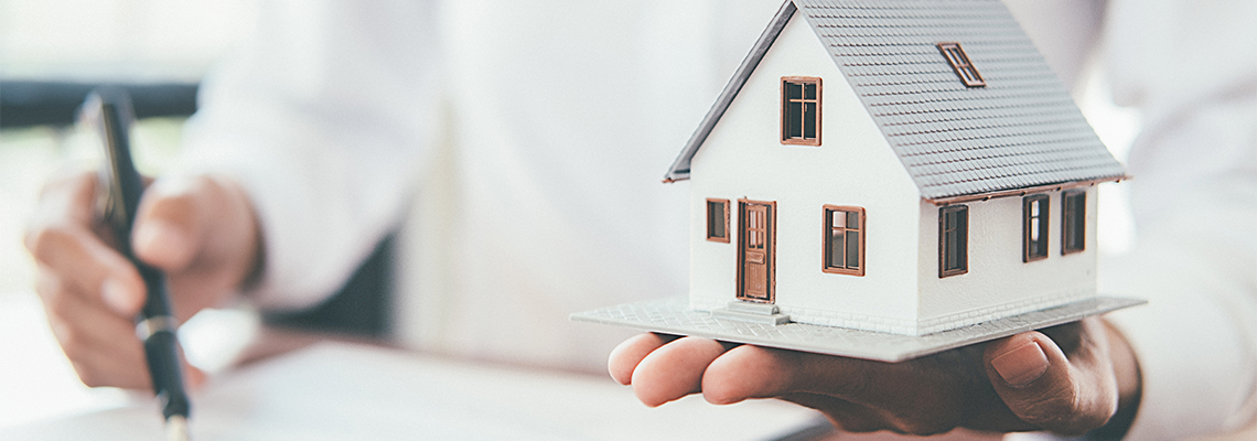 Man holding house model and discussing mortgage with real estate agent