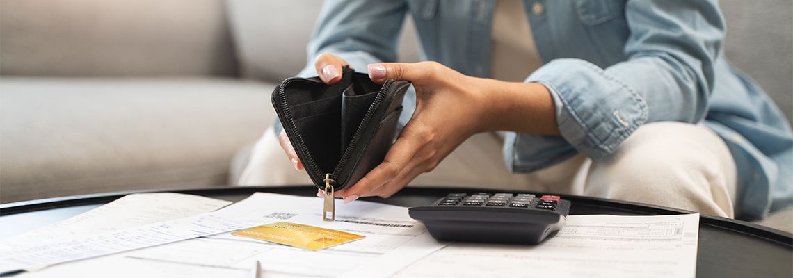 Person sits on couch with empty wallet and unpaid bills