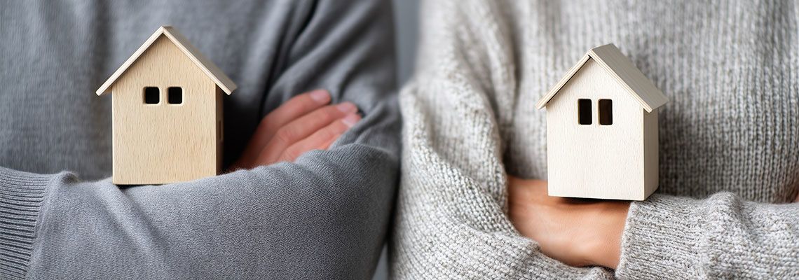 Man, and women holding separate wooden house symbolizing property division