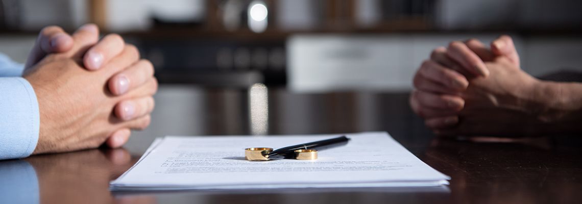 Couple sitting at table with clenched hands near divorce documents