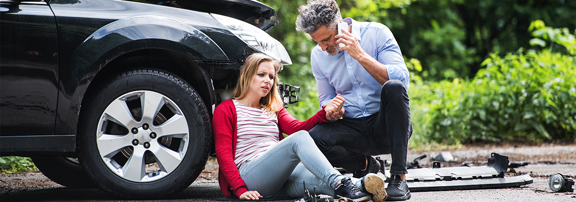 Young woman by the car after an accident and a man making a phone call