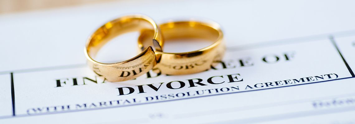 Two broken golden wedding rings on top of divorce paper