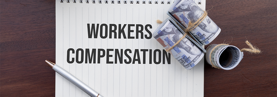 A financial notebook marked 'Workers Compensation' with bundled cash resting nearby