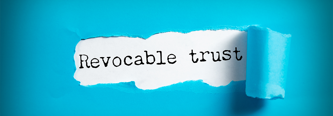 A hand holding a pen writes Revocable trust