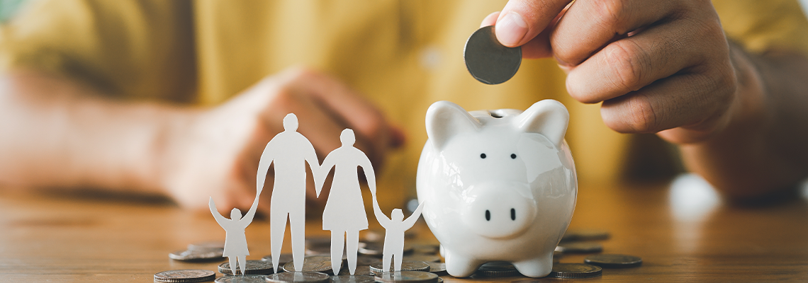 Businessman putting coin on the piggybank and paper family on table