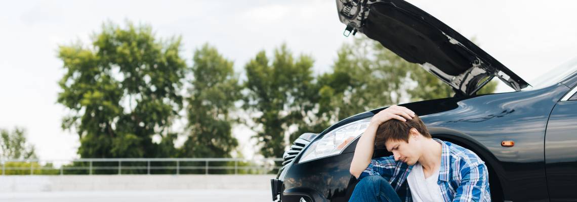 Man sitting on road with broken car