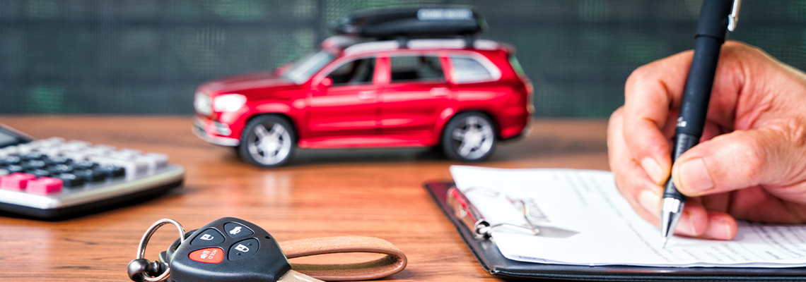 Car key on table with a man signing on leasing or document form and red car