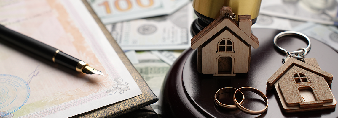 Gold wedding rings, wooden house model, and a judge gavel on legal paperwork