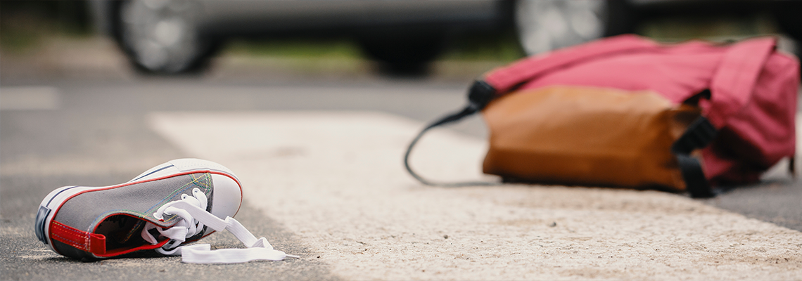 Car accident concept - an empty crosswalk with a child's shoe and backpack lying on the road