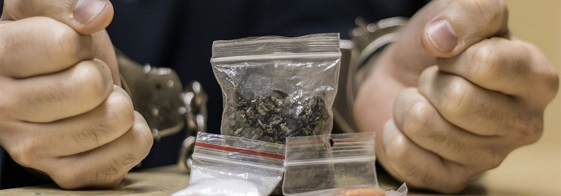 Handcuffed man with drugs on table