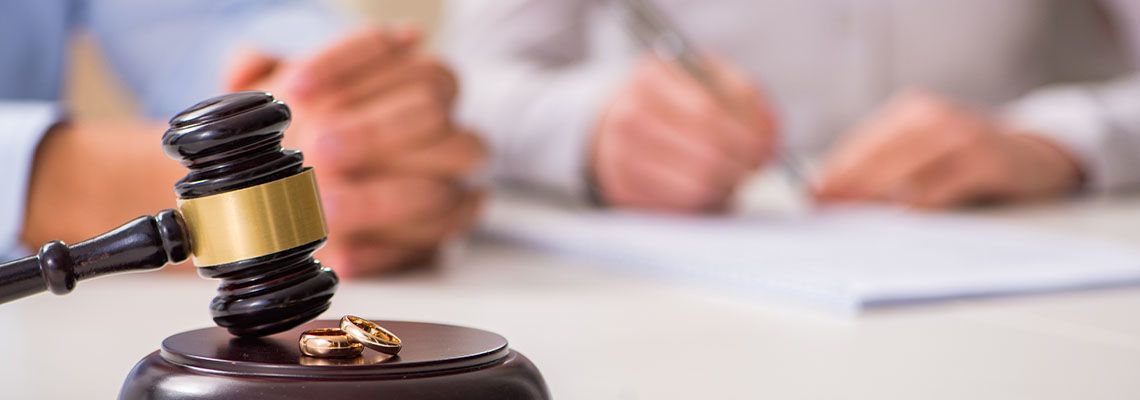 Wedding rings on gavel and a couple signing papers in background