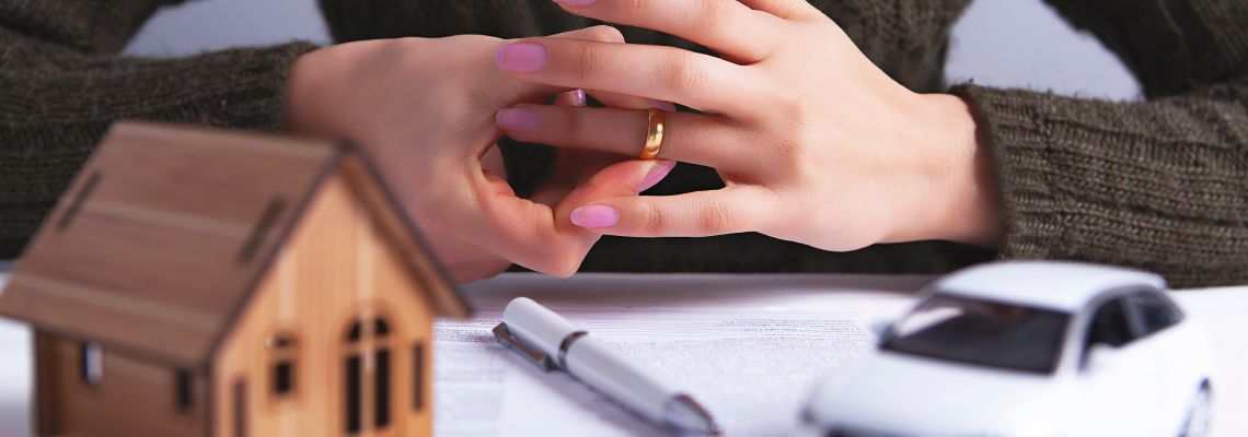Miniature house, car on table with women removing wedding ring from hand