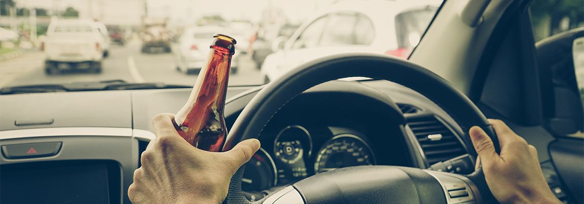 Man driving car with beer bottle in hand