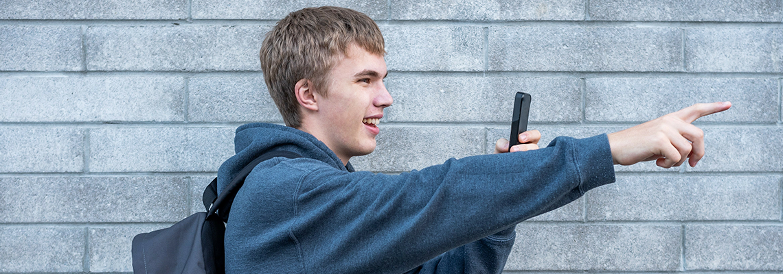 Teenager pointing to something he is recording with his cellphone.