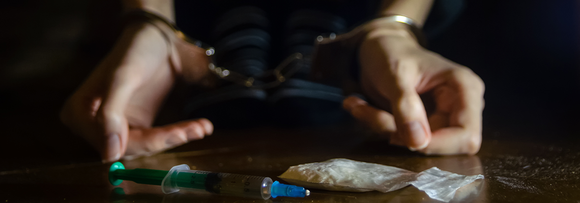 Syringe and Drugs with Man on The Floor and His Hands on Handcuffs