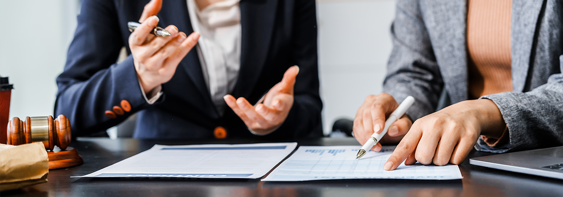 Female lawyers in business suits meet at wooden desk, shaking hands over contract paper