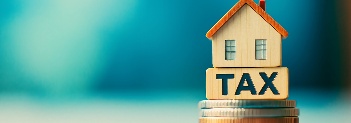 A wooden house model sits atop a stack of coins marked "TAX,"