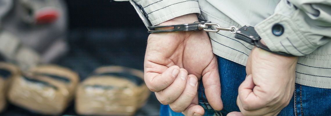 Handcuffed man with pouch of drugs in background