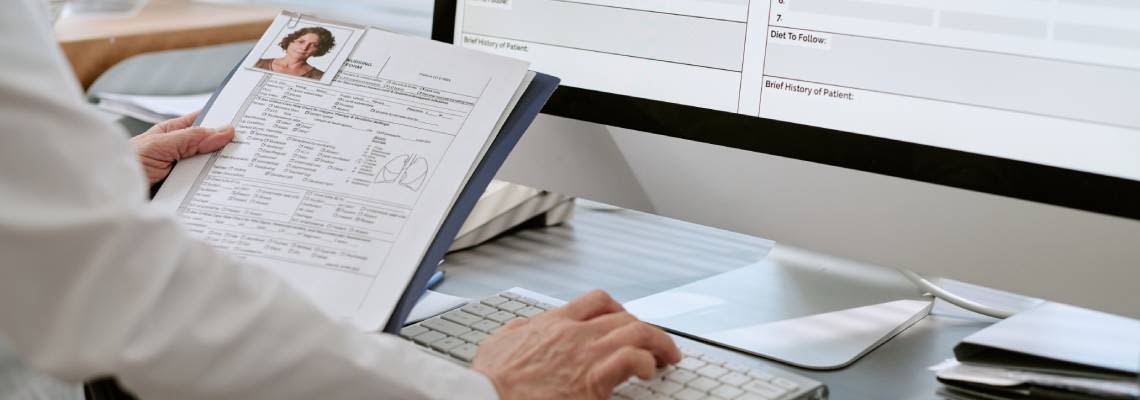 Worker reviewing patient file and entering medical data into electronic records