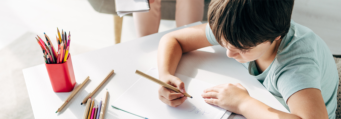 Panoramic shot of kid with dyslexia drawing on paper with pencil