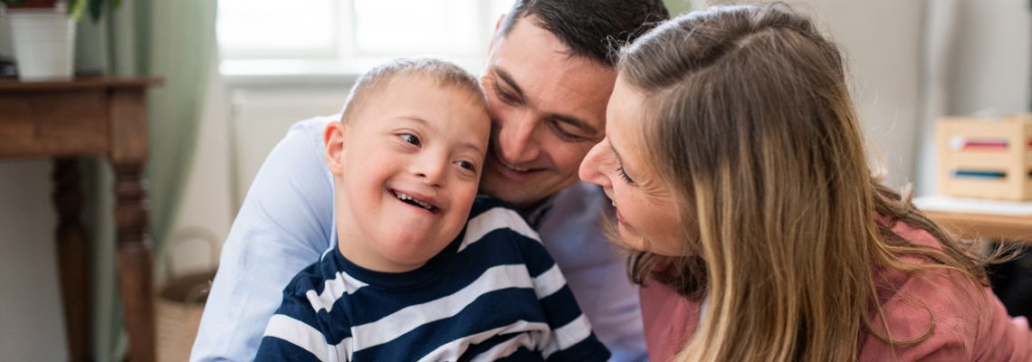 Cheerful down syndrome boy with parents indoors at home