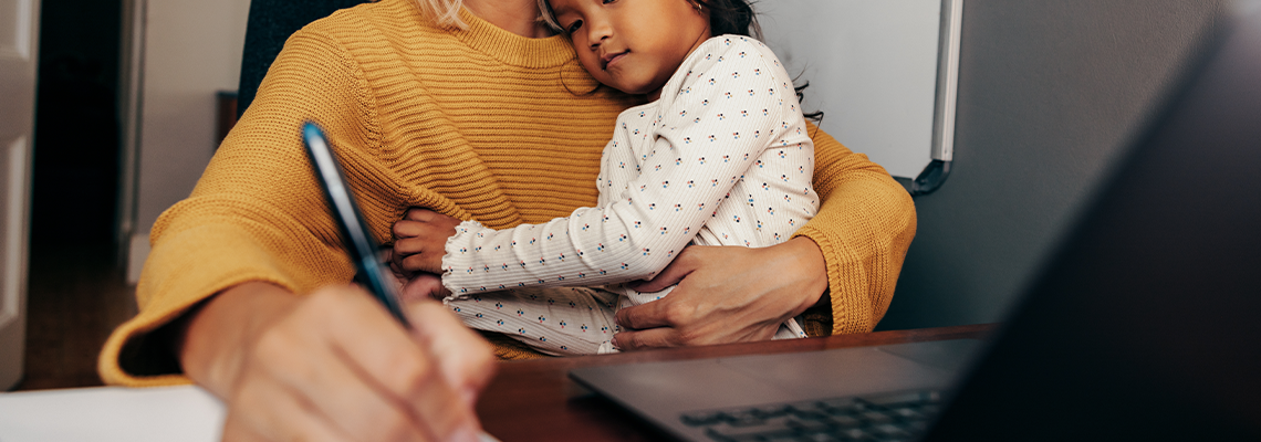 Young working mom writing notes while embracing her daughter