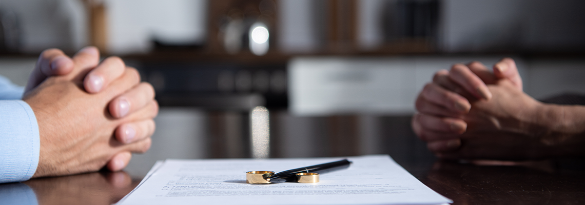 Partial view of couple sitting at table with clenched hands near divorce documents