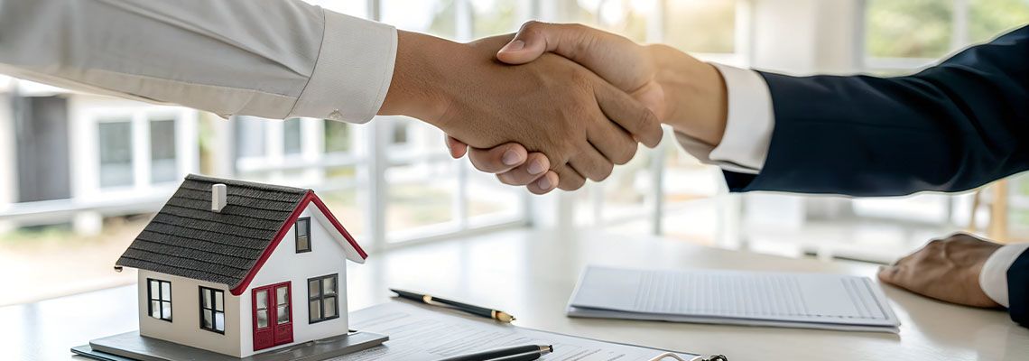 People shaking hand with miniature house and contract on table