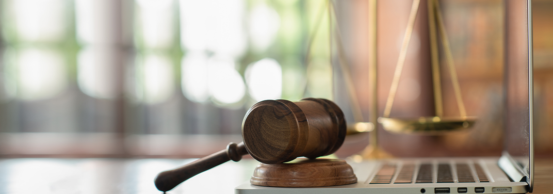 Judge gavel on computer with scales of justice on desk
