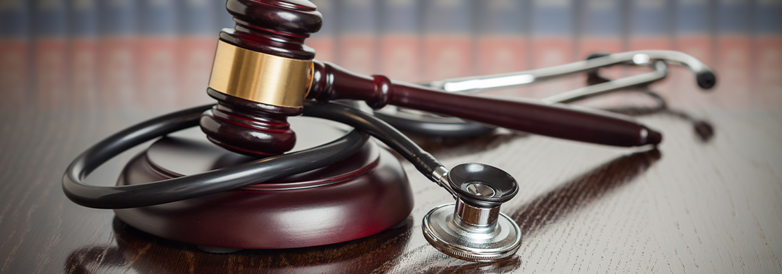 Gavel and Stethoscope on Wooden Table With Law Books In Background