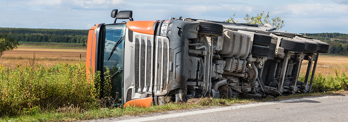 Overturned truck in field next to road, chassis visible
