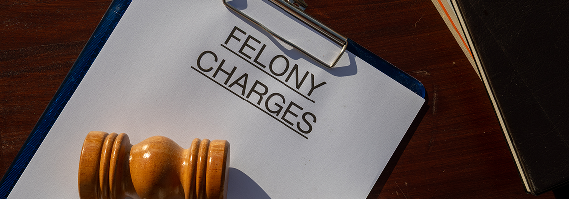 A felony charges paper secured in a clipboard, placed with a gavel