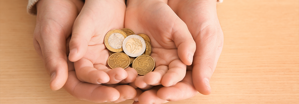 Hands of young man and his son holding coins on wooden table