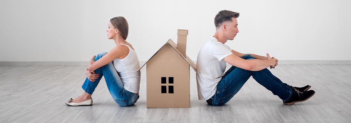 Angry couples sitting opposite of each other with model house in middle