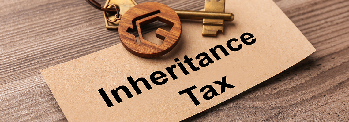 Card and key with key chain in shape of house on wooden table and text 'Inheritance Tax'