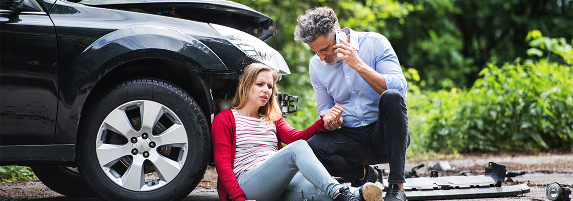 Young woman by the car after an accident and a man making a phone call