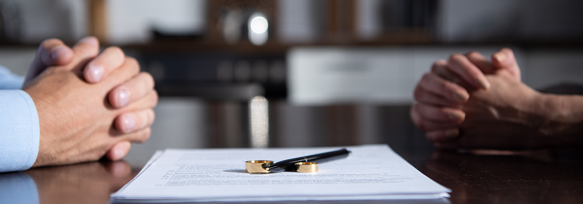Partial view of couple sitting at table with clenched hands near divorce documents