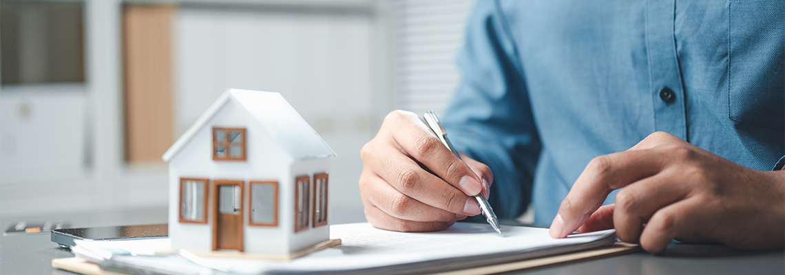 A professional signing real estate documents beside a small house mode