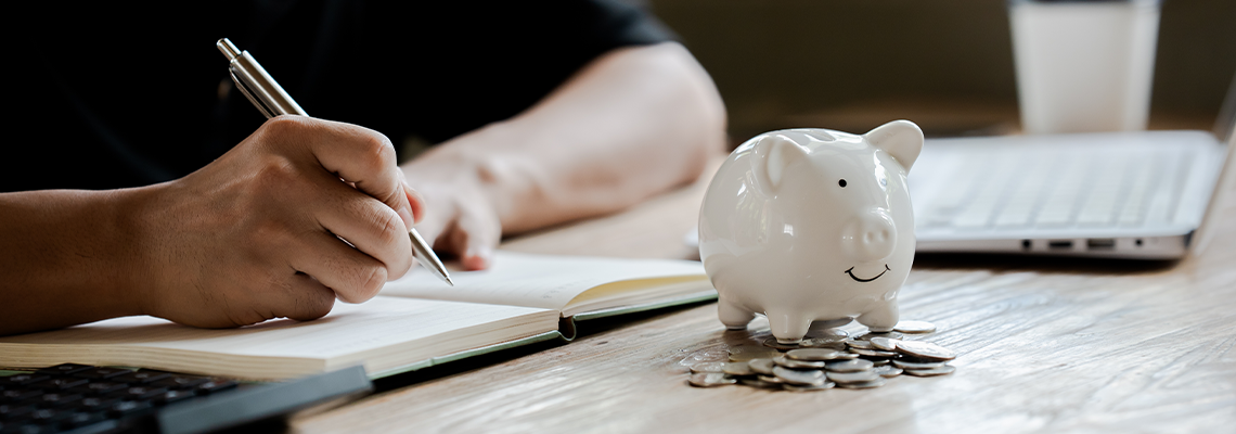 Person putting a coin into a piggy bank while using a calculator