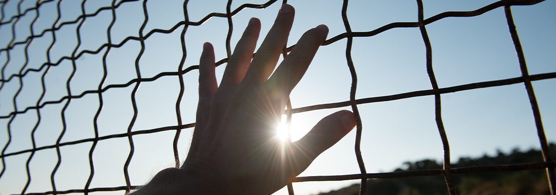 Human hand touching fence cage in jail and illegal immigration on sunset